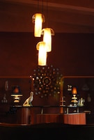 Zona bar con banconi in legno, lampade a sospensione e un elemento decorativo a parete.