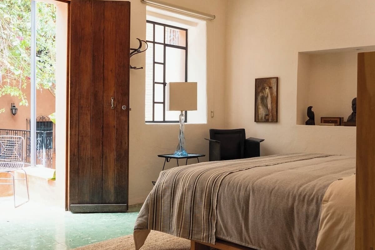 Quarto com cama, janela, abajur e porta que dá para área externa.