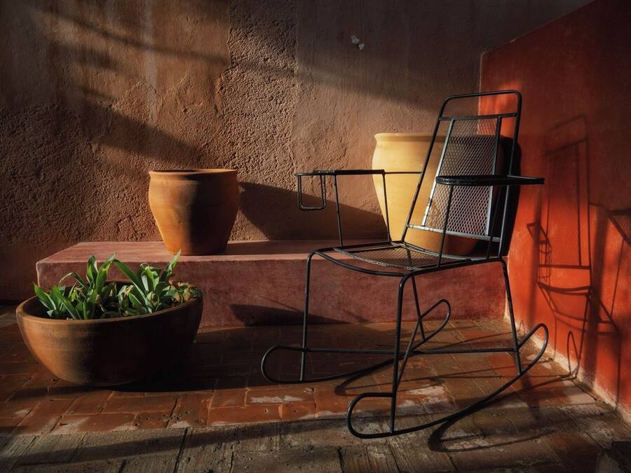 Un espacio de estar al aire libre de estilo rústico con una silla de metal, macetas de terracota y una planta en maceta.