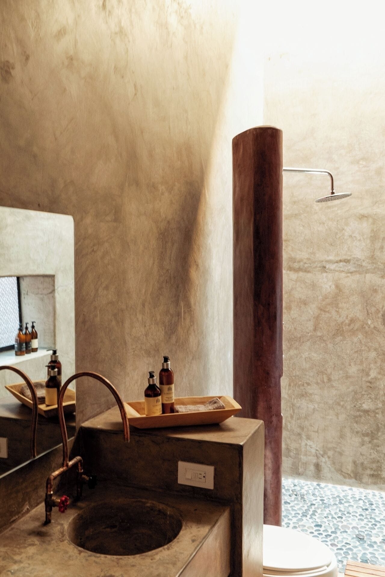 Un baño con un lavabo de madera grande, un espejo y una ducha con un pilar de madera.