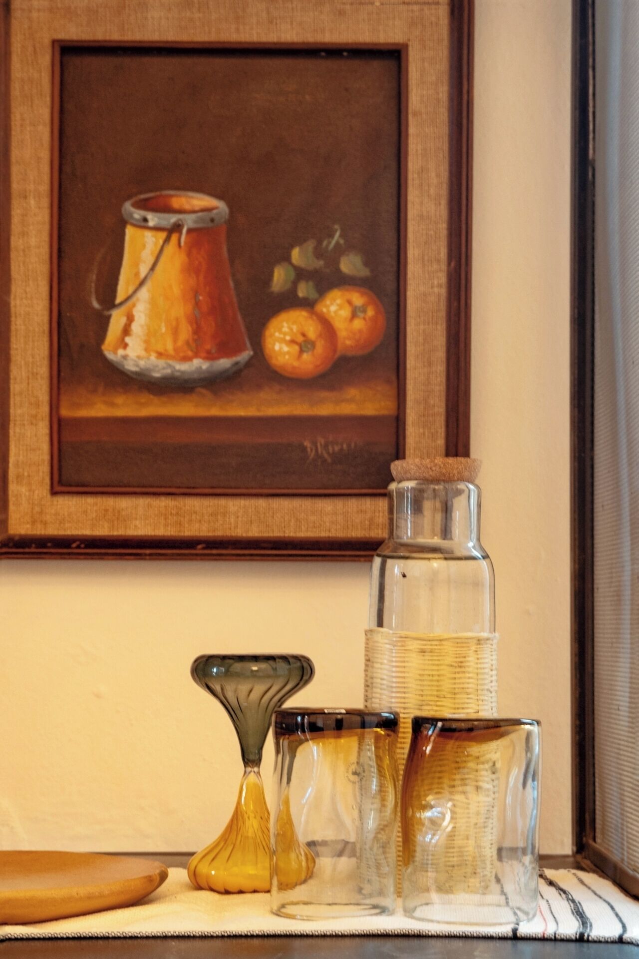 Ein gerahmtes Bild von einer Tonne und Orangen an einer Wand, eine Reihe von klaren Glasbehältern und eine kleine Vase auf einem Tisch.