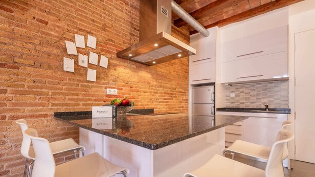 A modern kitchen with a brick wall, stainless steel appliances, and a central island with bar stools.