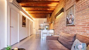 A modern living room with a brick wall, a sofa, a coffee table, and a kitchen area in the background.