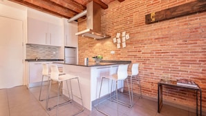 A modern kitchen with a brick wall, white cabinetry, and a central island with bar stools.
