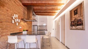 Une cuisine moderne avec un mur en briques, des appareils électroménagers en acier inoxydable et un coin repas avec des chaises blanches.