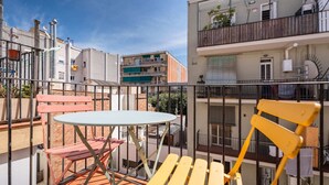 Un balcon avec une table et des chaises, donnant sur un quartier résidentiel avec des immeubles et un ciel dégagé.
