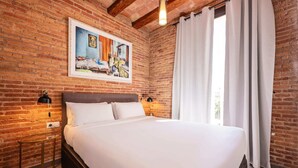 Une chambre d’hôtel avec un mur en briques, un grand lit, deux lampes de chevet et une fenêtre avec des rideaux.