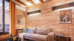 Un salon chaleureux avec un mur en briques, un canapé beige et une petite table d’appoint.