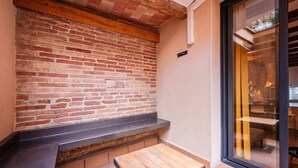 Un mur de briques avec un banc en bois et une petite table, une porte-fenêtre coulissante et un sol carrelé.