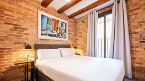 Une chambre avec un mur en briques, un grand lit, deux lampes de chevet et une fenêtre avec des rideaux.