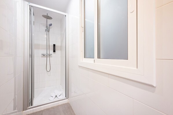 A glass-enclosed shower with a handheld showerhead and a wall-mounted faucet.