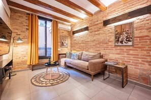 A cozy living room with exposed brick walls, a wooden ceiling, and a large window with curtains.