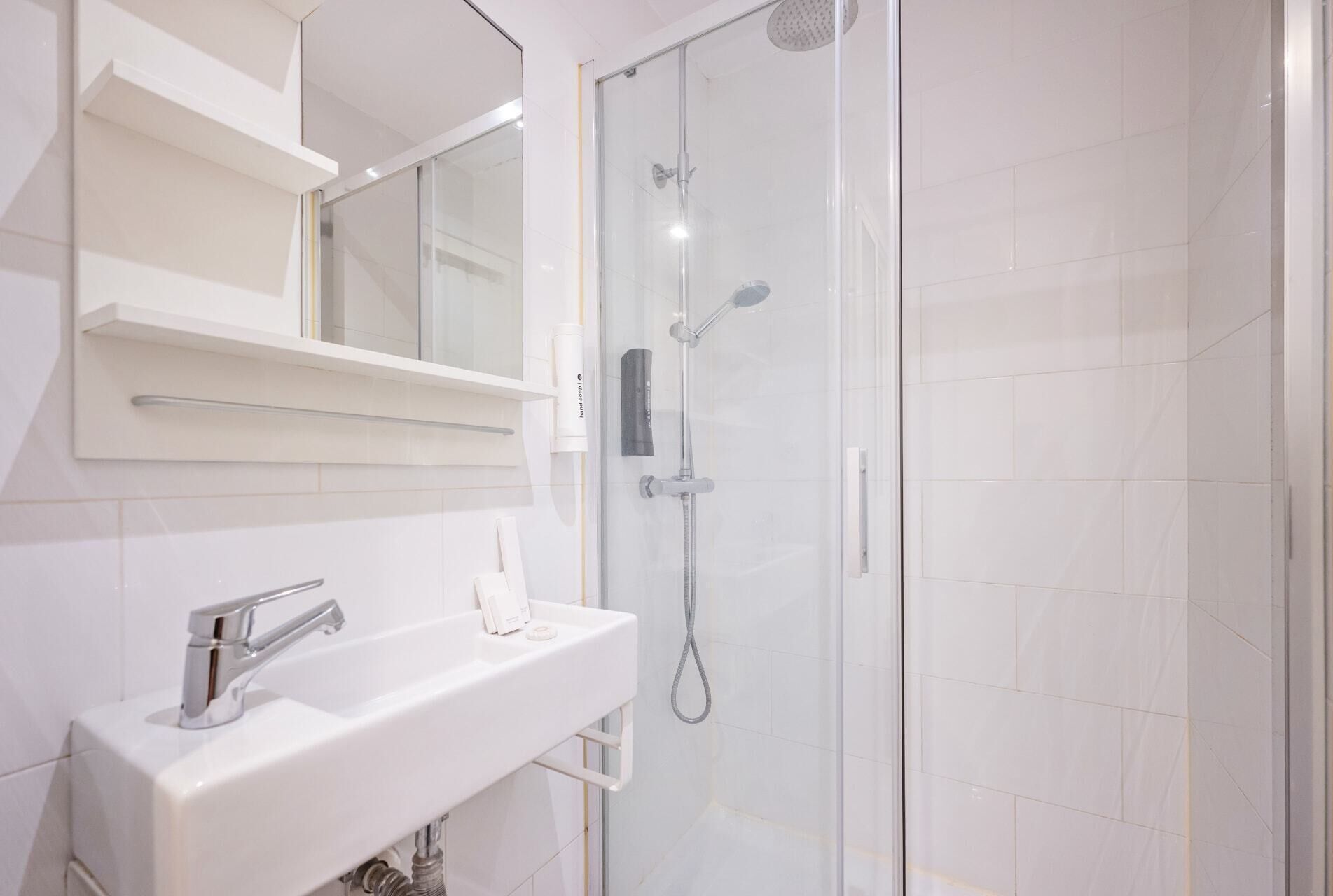 A modern bathroom with a white sink, mirror, and glass-enclosed shower.