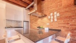 A modern kitchen with a central island, white bar stools, and a brick wall with a decorative light fixture.