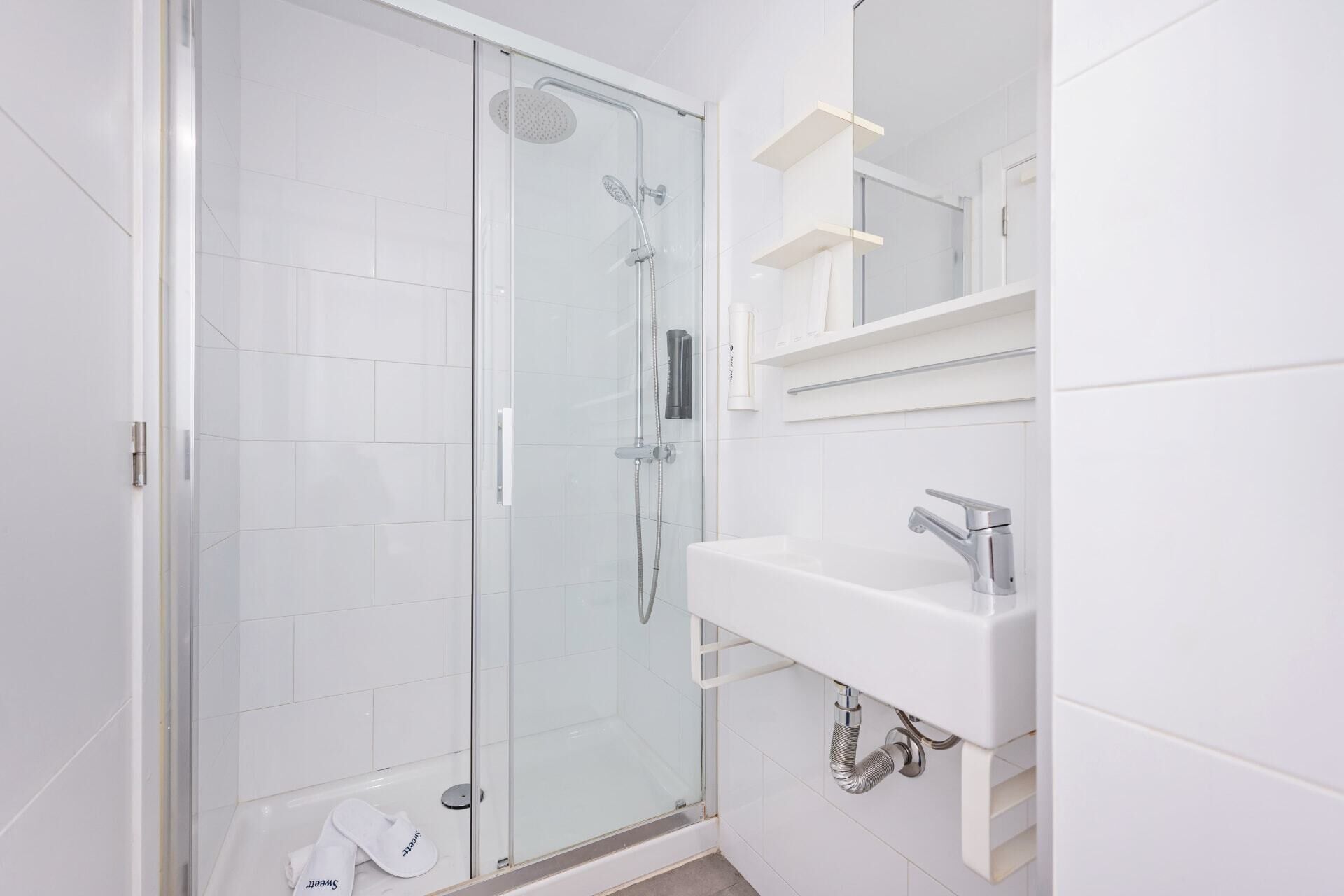 A modern bathroom with a glass-enclosed shower, a white sink, and a mirror above it.