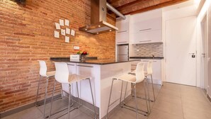 A kitchen with a brick wall, white cabinets, stainless steel appliances, and three white bar stools.