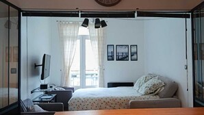 A modern bedroom with a wooden bed, a desk with a computer, a clock, and a window with curtains. - FI Bis Saint Malo (Saint-Malo)