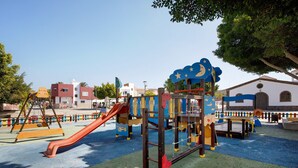 A playground with slides and climbing structures, surrounded by buildings and trees. - Holidays 'La Lajita Beach Studio' with Sea View, Wi-Fi and Air Conditioning (La Lajita)