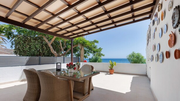 A covered patio with wicker furniture, a glass table, and a wall decorated with plates. - Holidays 'La Lajita Beach Studio' with Sea View, Wi-Fi and Air Conditioning (La Lajita)
