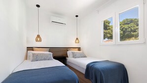 A bedroom with two beds, a wooden headboard, a window with a view of trees, and an air conditioning unit. - Holidays 'La Lajita Beach Studio' with Sea View, Wi-Fi and Air Conditioning (La Lajita)