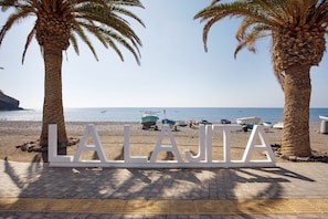 A beach with palm trees and boats, and a sign that reads 'LAJJA'.
