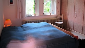 Een slaapkamer met een bed, een raam met gordijnen, een radiator, een stoel en houten kasten.