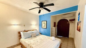 A bedroom with a bed, a ceiling fan, a wall-mounted light, and a door leading to another room. - Best Location in Vieques! Studio/Steps to Ocean, Biobay, Restaurants and Beaches (Esperanza)