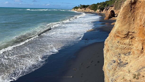 A beach with clear blue water, a sandy shore, and a rocky cliff. - Best Location in Vieques! Studio/Steps to Ocean, Biobay, Restaurants and Beaches (Esperanza)