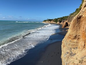 A beach with clear blue water, a sandy shore, and a rocky cliff. - Best Location in Vieques! Studio/Steps to Ocean, Biobay, Restaurants and Beaches (Esperanza)