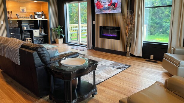 A modern living room with a fireplace, a television, and a large window with a view of greenery.