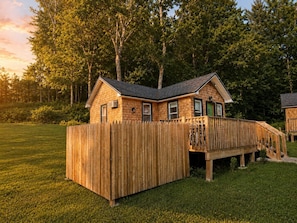A wooden cabin with a deck, surrounded by a grassy yard and trees. - Catskill Tiny Home, King Bed & Hot Tub on 18 acres (Ellenville)