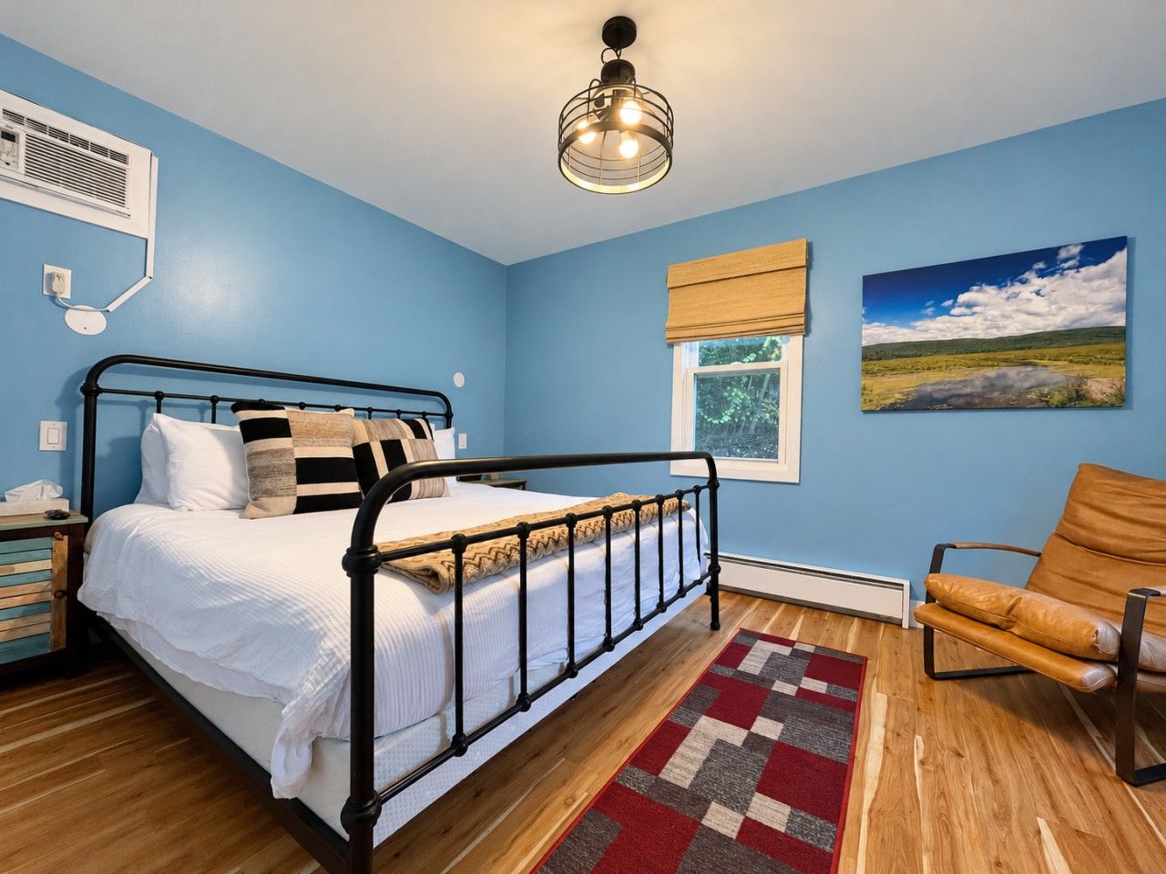 A bedroom with a bed, a chair, a window, and a painting on the wall.