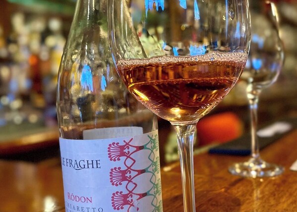 A bottle of wine with a label and a glass of red wine on a bar counter.