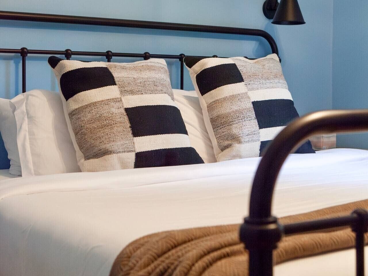 A bed with a metal frame, white bedding, and two checkered pillows.