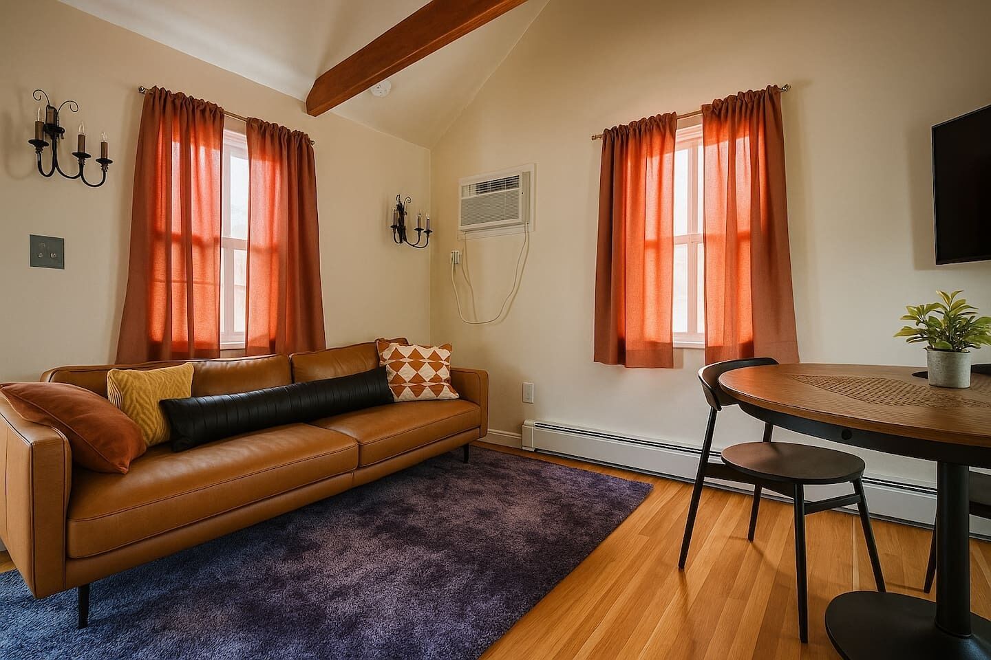 A room with a brown leather sofa, a round wooden table with two chairs, and a potted plant on the table.