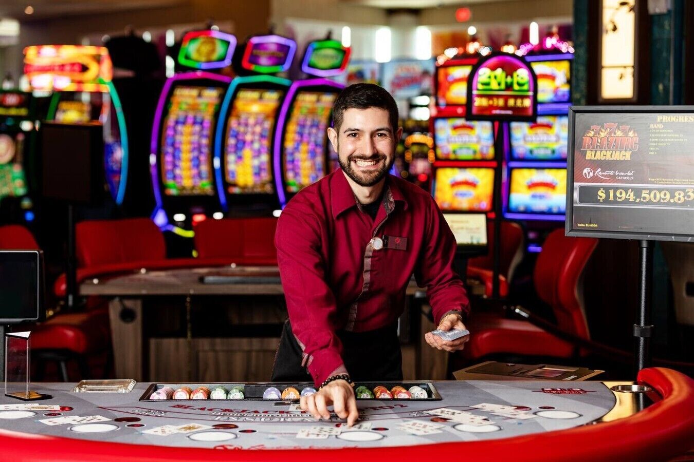 Ein Kasinobereich mit einem Blackjack-Tisch, mehreren Spielautomaten und einer Person, die hinter dem Tisch steht.