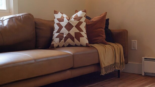 Un canapé en cuir marron agrémenté de coussins à motifs et d’un plaid.
