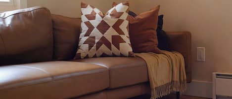 A brown leather sofa with patterned pillows and a throw blanket.
