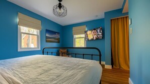 Une chambre à coucher avec un lit, un tableau, une télévision et une fenêtre avec des rideaux.