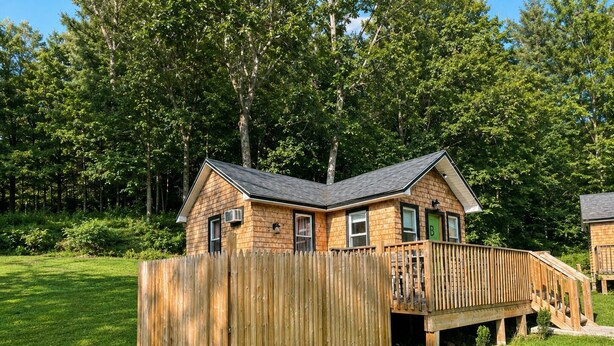 Une cabane en bois dotée d’une terrasse et d’un espace clos, entourée d’une forêt.