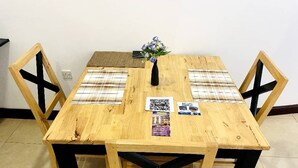 A wooden dining table with a black cross-back chair, a vase with flowers, and a QR code on the table. - Amaryllis Residences Mount Pleasant (Blantyre)