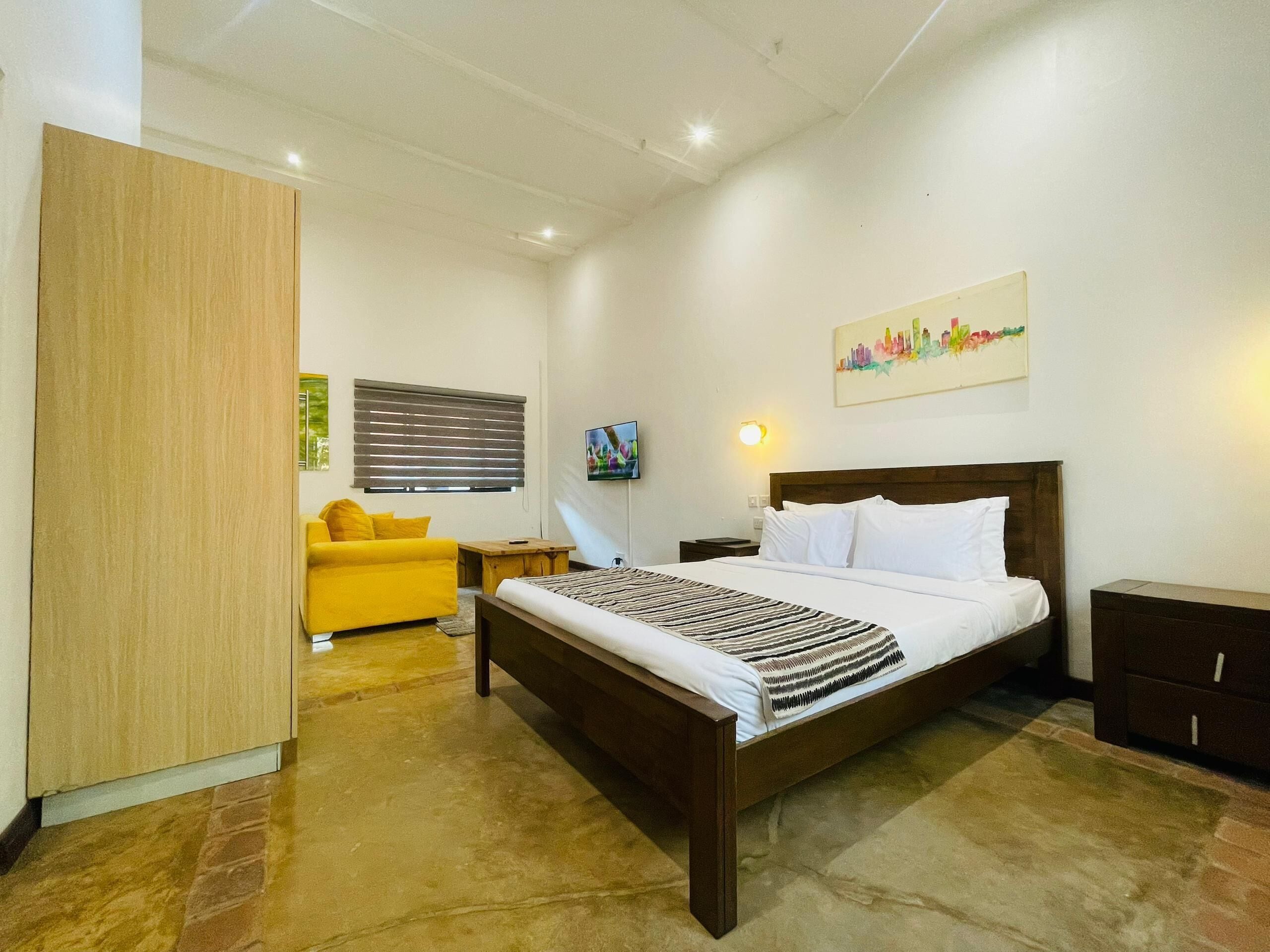 A hotel room with a bed, a sofa, a wooden wardrobe, a TV, and a painting on the wall.