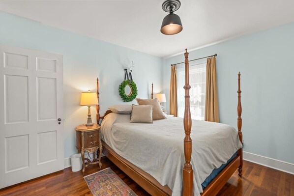 Une chambre à coucher avec un lit à baldaquin, une table de chevet avec une lampe, une guirlande décorative accrochée au mur et un plancher en bois.