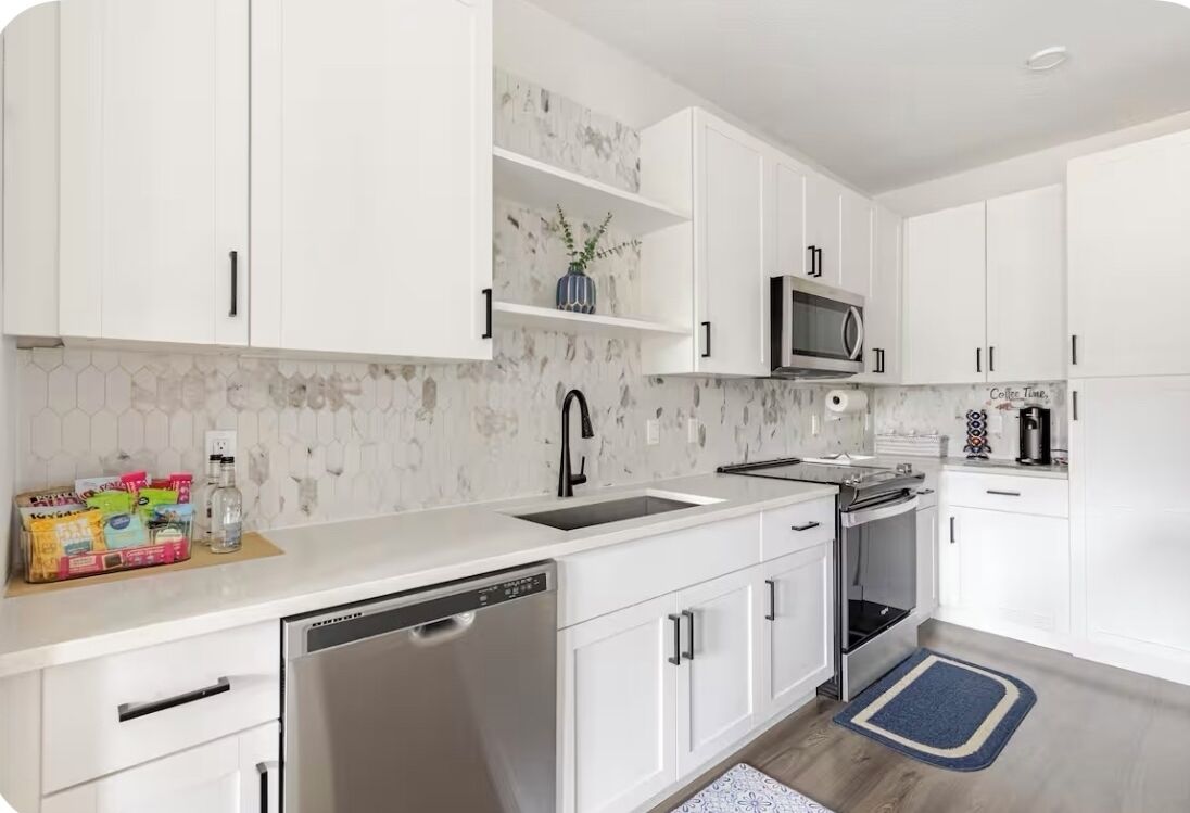 A modern kitchen with white cabinets, a stainless steel dishwasher, a microwave, and an oven.