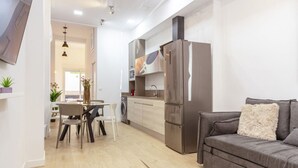 Una cucina moderna con frigorifero in acciaio inossidabile, zona pranzo con tavolo e sedie e un divano grigio.