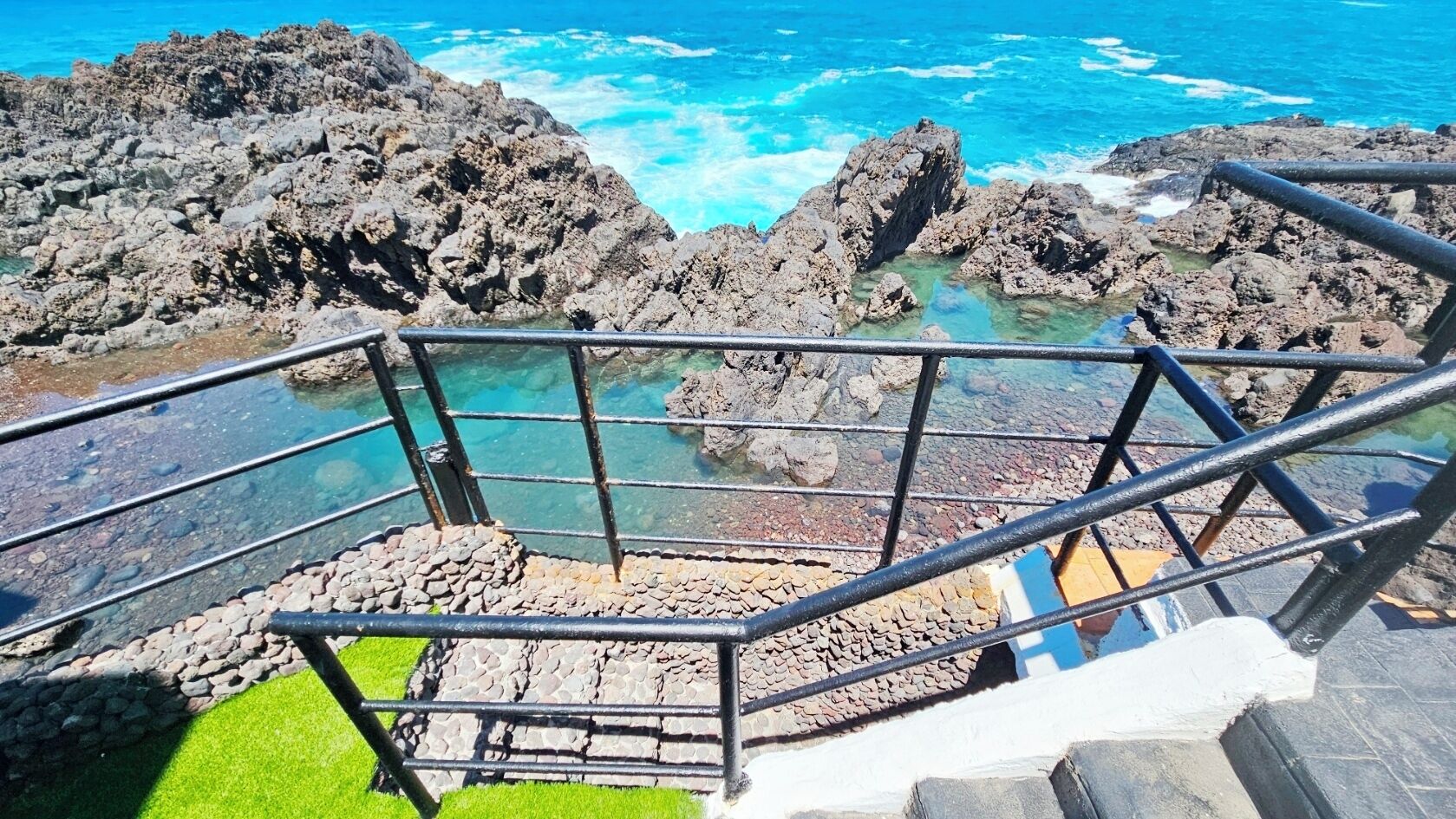 A staircase leading to a rocky coastline with clear blue waters.