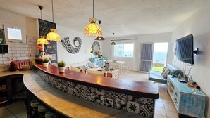 A spacious living area with a curved wooden bar, a large decorative wall, and a view of the sea through a sliding door. - House on the seafront (La Matanza de Acentejo)