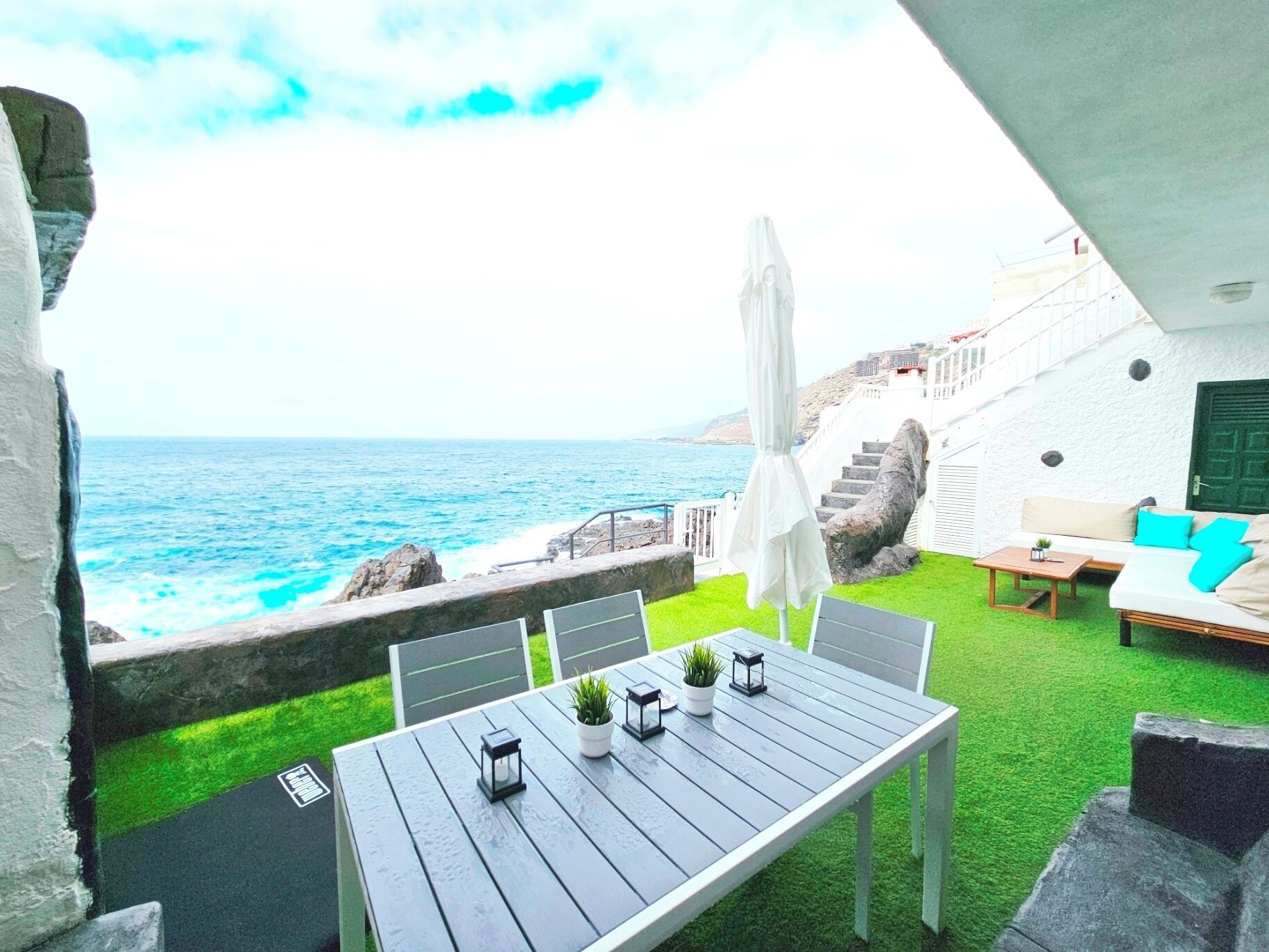 Eine Terrasse mit Tisch und Stühlen, ein weißes Sofa mit blauen Kissen und Blick auf den Ozean.