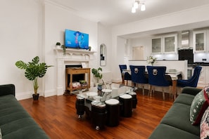 Een moderne woonkamer met een open haard, een televisie en een eethoek met blauwe stoelen.