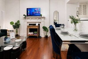 Een moderne woonkamer met een open haard, een eethoek voor vier personen, en een televisie boven de haard.